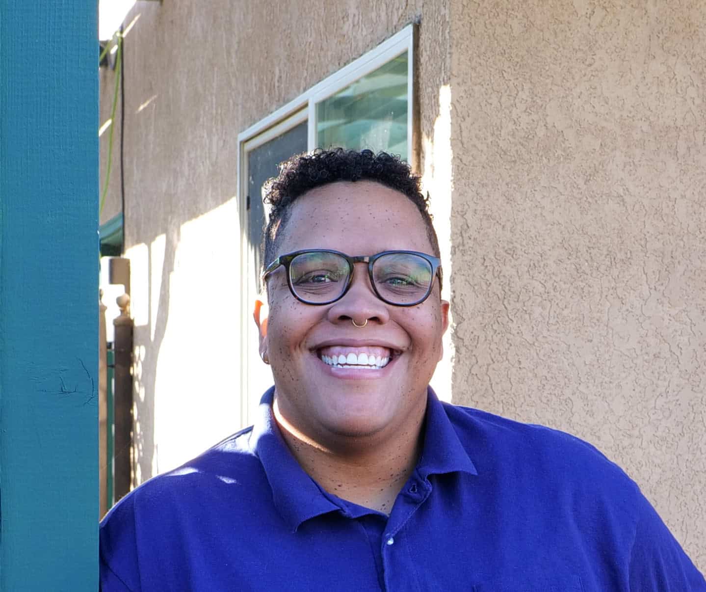 Smiling woman with short coily hair and glasses wearing a blue collared shirt