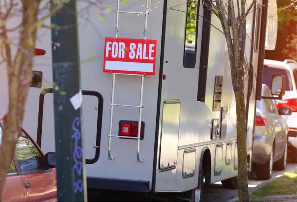 RV parallel parked on city street with for sale sign attached to its ladder
