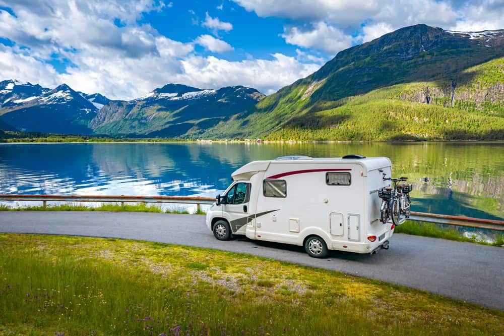 RV driving on a winding road next to an alpine lake