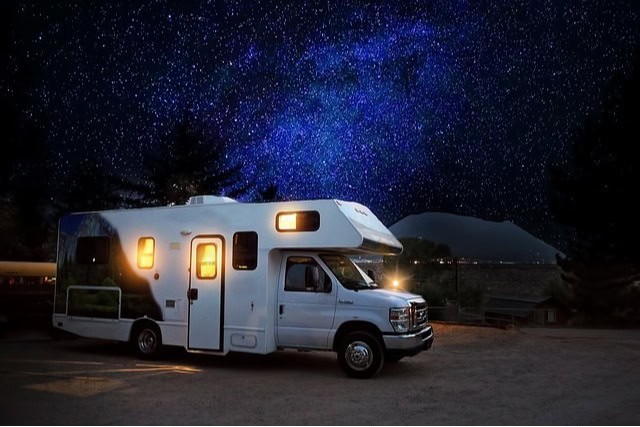 RV with interior lights turned on against a beautiful, starry night sky. RV water heater.
