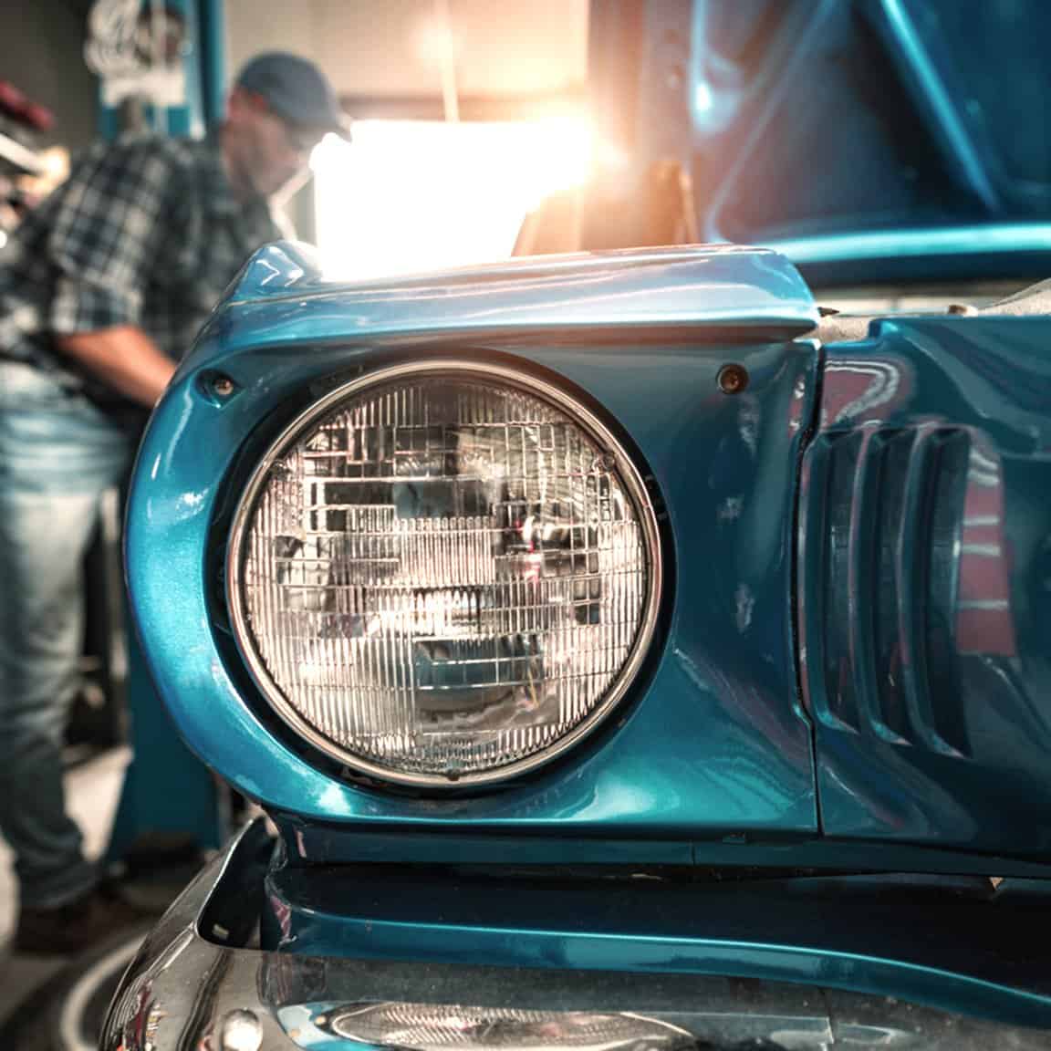 Man working on classic car in a storage unit.