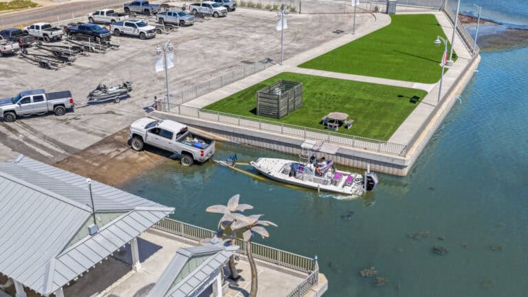 Luxury waterfront parking and boat dock area with green lawn and shaded seating.