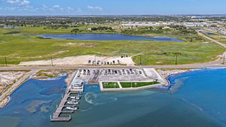 Drone view of Outrig marina with boats, waterfront park, and parking area.