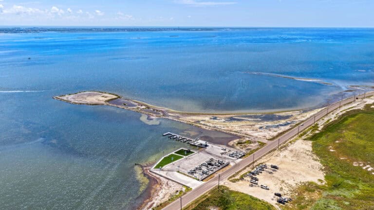 Seaside marina with boat docks, parking, and green spaces overlooking a large coastal body of water.