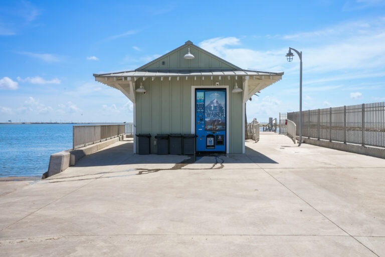 Vending machine on pier with water and sky in background, at an outdoor waterfront at Outrig Corupus Christi