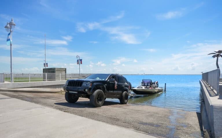 Jeep towing a boat at a marina on a sunny day with a clear blue sky.