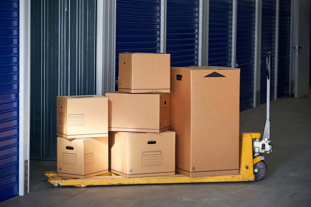 Stacked cardboard boxes on a yellow hand truck in a storage unit or warehouse.