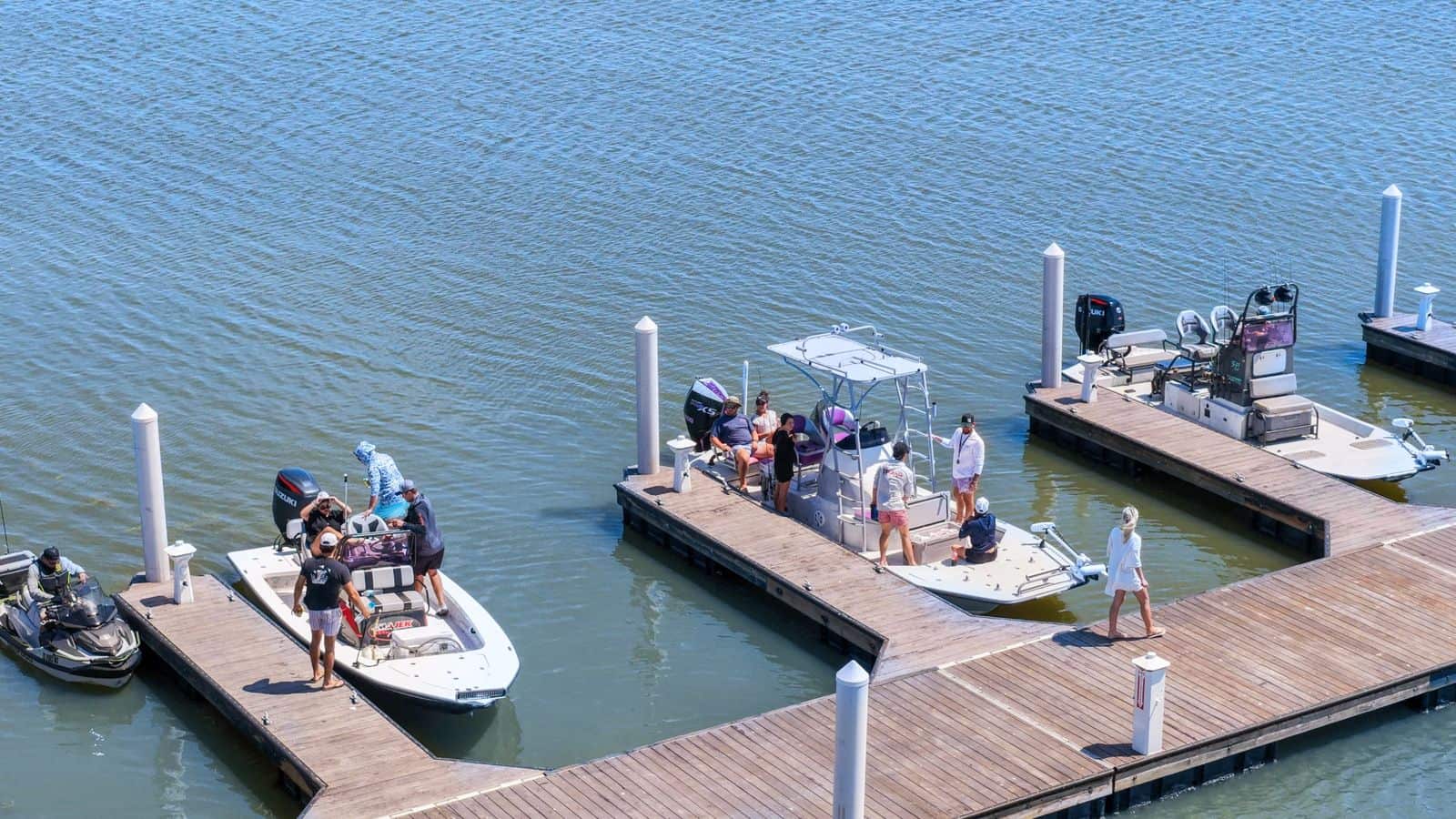 Boats docked at marina with people enjoying a day on the water, watercrafts, and a wooden pier in a scenic harbor.